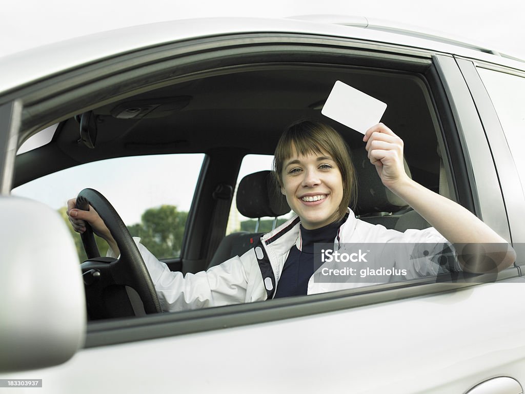 Young beautiful woman sitting in a new car and holding a blank empty sign/ driving licence/ credit card.